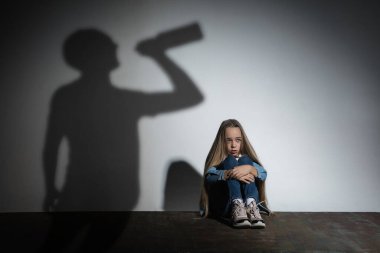 Aile içi şiddet, istismar. Korkmuş küçük beyaz kız, beyaz duvarın yanında oturan, alkol bağımlısı kızgın bir babanın gölgesi..