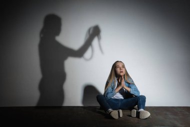 Aile içi şiddet, istismar. Korkmuş küçük beyaz kız, beyaz duvarın yanında oturan kızgın annelerin gölgesiyle tehdit eden kurban..