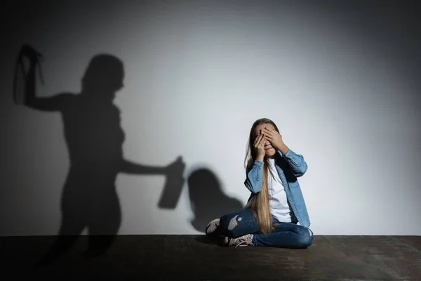 Бытовое насилие, насилие. Испуганная маленькая кавказская девочка, жертва сидит у белой стены с тенью злобной угрожающей матери с алкогольной зависимостью. — стоковое фото