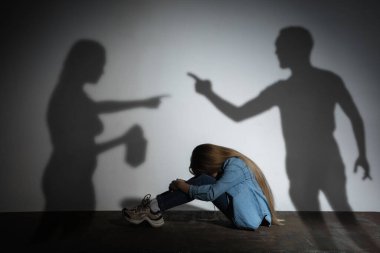 Aile içi şiddet, istismar. Korkmuş küçük beyaz kız, beyaz duvarın yanında oturan alkol bağımlısı kızgın ebeveynlerin gölgesi altında.