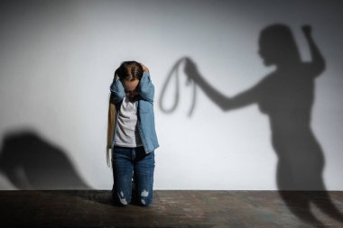 Aile içi şiddet, istismar. Korkmuş küçük beyaz kız, beyaz duvarın yanında oturan kızgın annelerin gölgesiyle tehdit eden kurban..