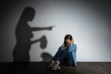 Aile içi şiddet, istismar. Korkmuş küçük beyaz kız, beyaz duvarın yanında oturan, alkol bağımlısı, tehdit eden anne gölgesi olan kurban..
