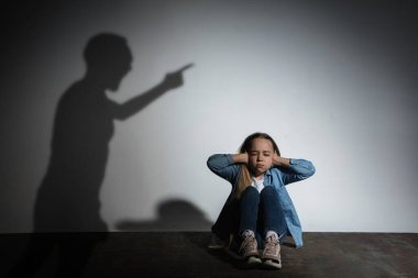 Aile içi şiddet, istismar. Korkmuş küçük beyaz kız, beyaz duvarın yanında oturan kızgın babaların gölgesi altında.