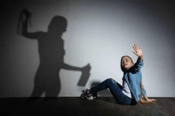 Przemoc domowa, molestowanie. Wystraszona mała biała dziewczynka, ofiara siedząca blisko białej ściany z cieniem wściekłej, groźnej matki z uzależnieniem od alkoholu. — Zdjęcie stockowe