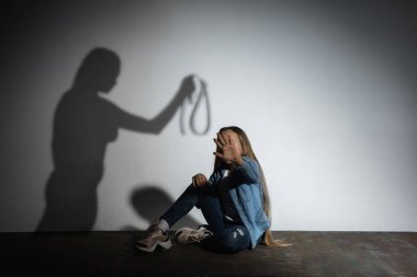 Aile içi şiddet, istismar. Korkmuş küçük beyaz kız, beyaz duvarın yanında oturan kızgın annelerin gölgesiyle tehdit eden kurban..