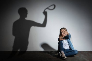 Aile içi şiddet, istismar. Korkmuş küçük beyaz kız, beyaz duvarın yanında oturan kızgın babaların gölgesi altında.