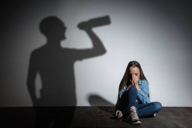 Aile içi şiddet, istismar. Korkmuş küçük beyaz kız, beyaz duvarın yanında oturan, alkol bağımlısı kızgın bir babanın gölgesi..