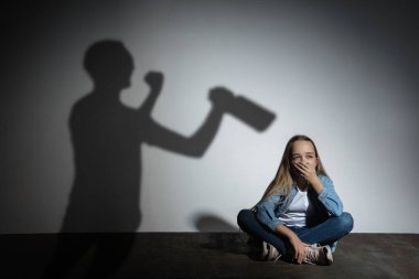 Aile içi şiddet, istismar. Korkmuş küçük beyaz kız, beyaz duvarın yanında oturan, alkol bağımlısı kızgın bir babanın gölgesi..