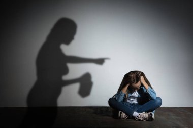Aile içi şiddet, istismar. Korkmuş küçük beyaz kız, beyaz duvarın yanında oturan, alkol bağımlısı, tehdit eden anne gölgesi olan kurban..