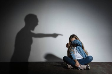 Aile içi şiddet, istismar. Korkmuş küçük beyaz kız, beyaz duvarın yanında oturan kızgın babaların gölgesi altında.