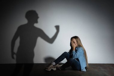 Aile içi şiddet, istismar. Korkmuş küçük beyaz kız, beyaz duvarın yanında oturan kızgın babaların gölgesi altında.
