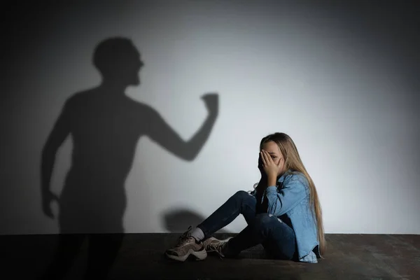 Häusliche Gewalt, Missbrauch. Verängstigtes kleines kaukasisches Mädchen, Opfer sitzt dicht an weißer Wand, auf der der Schatten wütender Väter droht. — Stockfoto