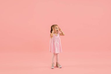 Çocukluk ve büyük ve ünlü bir gelecek hayal etmek. Mercan pembe arka planda izole edilmiş güzel uzun saçlı kız.