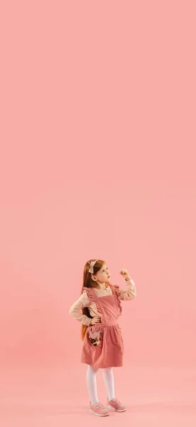 Infância e sonho sobre o futuro grande e famoso. Menina longhair bonita isolado no fundo rosa coral — Fotografia de Stock