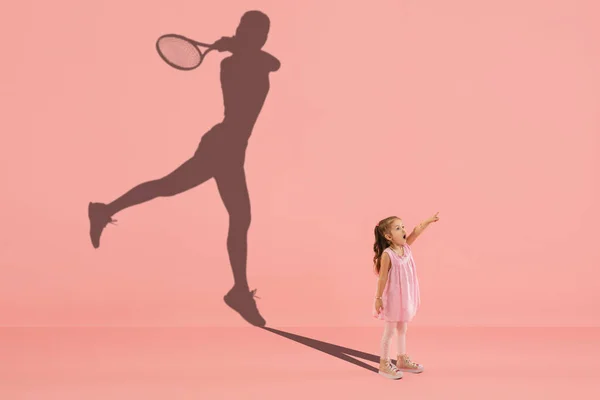 Παιδική ηλικία και όνειρο για μεγάλο και διάσημο μέλλον. Εννοιολογική εικόνα με το κορίτσι και τη σκιά του ταιριάζει θηλυκό τενίστα σε κοραλλιογενή ροζ φόντο — Φωτογραφία Αρχείου