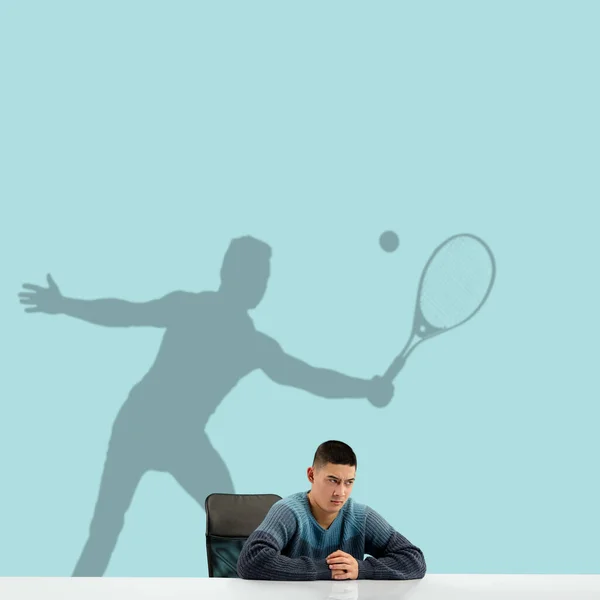 Jongeman droomt over de toekomst in de grote sport tijdens zijn werk in het kantoor. Een legende worden. Dromenschaduw op de muur achter hem. Kopieerruimte. — Stockfoto