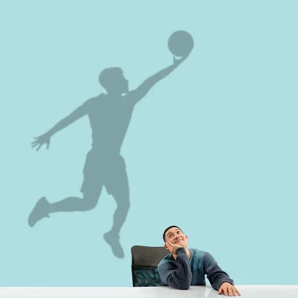 Молодой человек мечтает о будущем в большом спорте во время работы в должности. Стать легендой. Тень снов на стене позади него. Copyspace. — стоковое фото