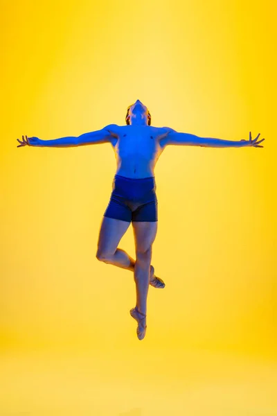 Jonge en sierlijke balletdanser geïsoleerd op gele studioachtergrond in neonlicht. Kunst, beweging, actie, flexibiliteit, inspiratie. — Stockfoto