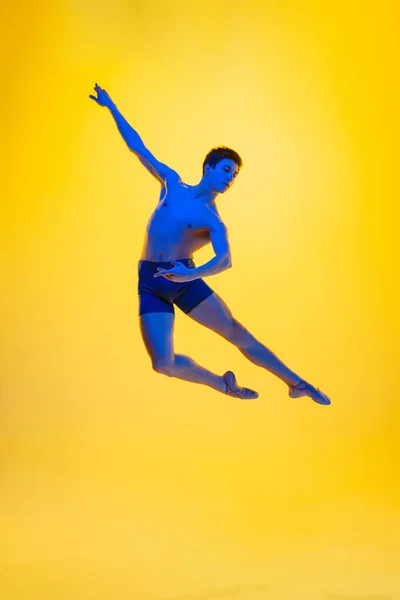 Jonge en sierlijke balletdanser geïsoleerd op gele studioachtergrond in neonlicht. Kunst, beweging, actie, flexibiliteit, inspiratie. — Stockfoto