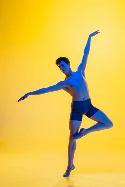 Jonge en sierlijke balletdanser geïsoleerd op gele studioachtergrond in neonlicht. Kunst, beweging, actie, flexibiliteit, inspiratie. — Stockfoto