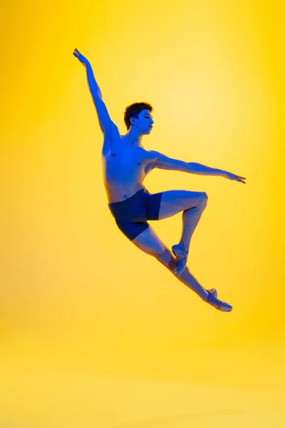 Молодая и изящная балетная танцовщица выделена на фоне желтой студии в неоновом свете. Искусство, движение, действие, гибкость, концепция вдохновения. — стоковое фото