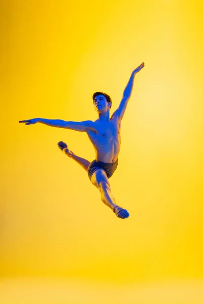 Jonge en sierlijke balletdanser geïsoleerd op gele studioachtergrond in neonlicht. Kunst, beweging, actie, flexibiliteit, inspiratie. — Stockfoto