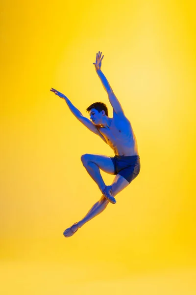 Jonge en sierlijke balletdanser geïsoleerd op gele studioachtergrond in neonlicht. Kunst, beweging, actie, flexibiliteit, inspiratie. — Stockfoto