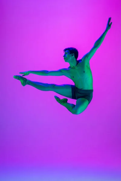 Jonge en sierlijke balletdanser geïsoleerd op paarse studioachtergrond in neonlicht. Kunst, beweging, actie, flexibiliteit, inspiratie. — Stockfoto