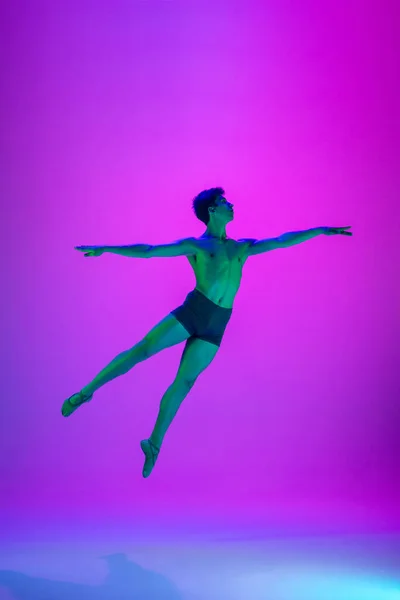 Молодая и изящная балетная танцовщица выделена на фиолетовом фоне студии в неоновом свете. Искусство, движение, действие, гибкость, концепция вдохновения. — стоковое фото