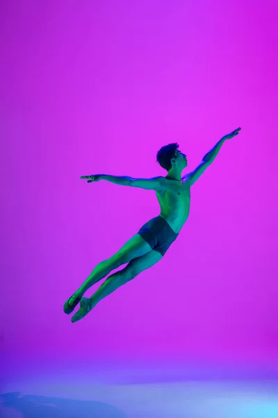 Jonge en sierlijke balletdanser geïsoleerd op paarse studioachtergrond in neonlicht. Kunst, beweging, actie, flexibiliteit, inspiratie. — Stockfoto