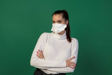 Yeşil stüdyo arka planında izole edilmiş koruyucu maskeli bir kadın. Yeni COVID kuralları önlemeyi yayıyor