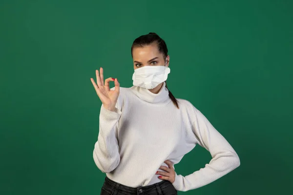 Mujer con mascarilla protectora aislada sobre fondo de estudio verde. Nuevas normas de prevención de la propagación de COVID — Foto de Stock