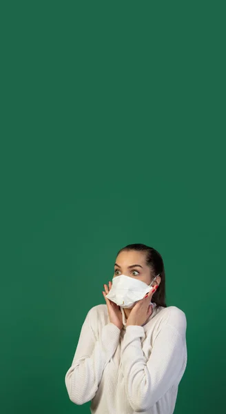 Mujer con mascarilla protectora aislada sobre fondo de estudio verde. Nuevas normas de prevención de la propagación de COVID — Foto de Stock