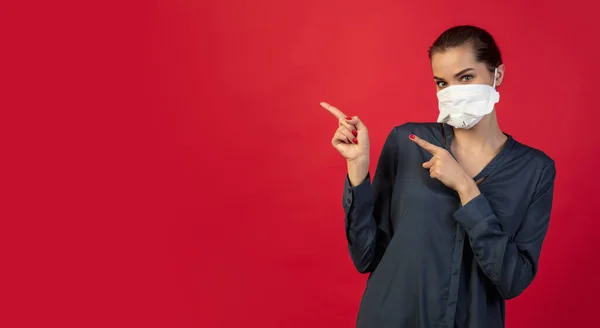 Mujer con mascarilla protectora aislada sobre fondo rojo estudio. Nuevas normas de prevención de la propagación de COVID — Foto de Stock