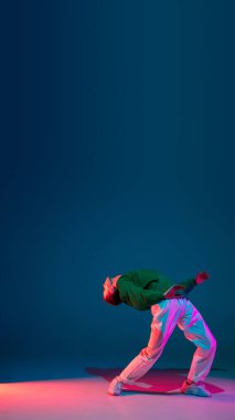 Renkli arka planda dans pistinde neon ışıklarıyla hip-hop dansı yapan şık sporcu çocuk. Gençlik kültürü, hareket, tarz ve moda, aksiyon.