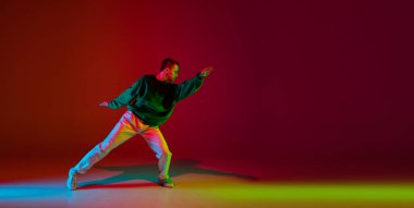 Renkli arka planda dans pistinde neon ışıklarıyla hip-hop dansı yapan şık sporcu çocuk. Gençlik kültürü, hareket, tarz ve moda, aksiyon.