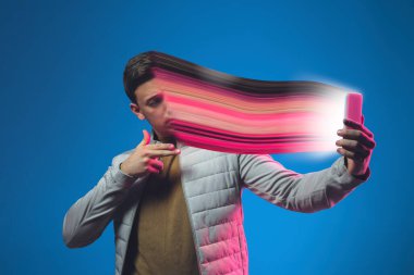Neon ışıklı iç mekânlı şık bir adamın sinematik portresi akıllı telefon kullanıyor. Yüzü dağılmış, telefonun içine çekilmiş. Sosyal ağ bağımlılığı kavramı
