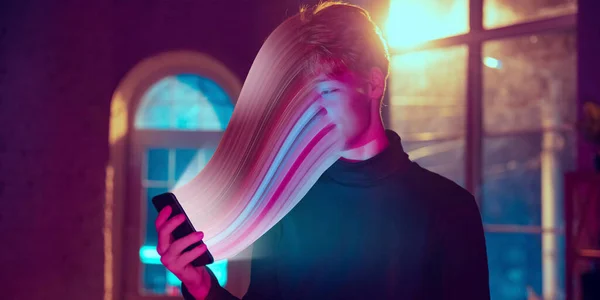 Filmový portrét stylového muže v neonově osvětleném interiéru pomocí chytrého telefonu. Tvář je rozmazaná, nasáklá do telefonu. Koncept závislosti na sociálních sítích — Stock fotografie
