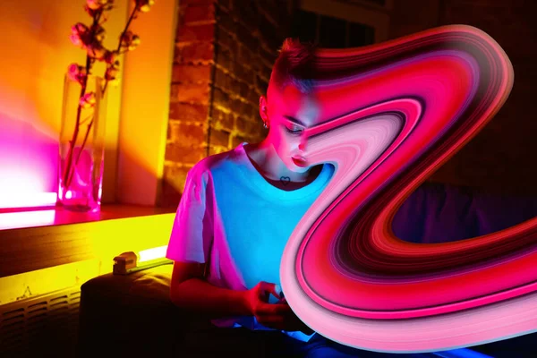 Filmový portrét stylové ženy v neonově osvětleném interiéru pomocí chytrého telefonu. Tvář je rozmazaná, nasáklá do telefonu. Koncept závislosti na sociálních sítích — Stock fotografie