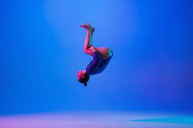 Genç esnek kız mavi stüdyo arka planında izole edilmiş. Genç bayan model sanatsal jimnastik yapıyor. Esneklik ve denge egzersizleri.