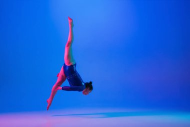 Genç esnek kız mavi stüdyo arka planında izole edilmiş. Genç bayan model sanatsal jimnastik yapıyor. Esneklik ve denge egzersizleri.