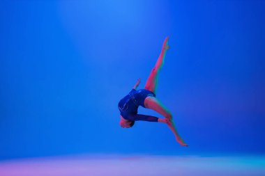 Genç esnek kız mavi stüdyo arka planında izole edilmiş. Genç bayan model sanatsal jimnastik yapıyor. Esneklik ve denge egzersizleri.