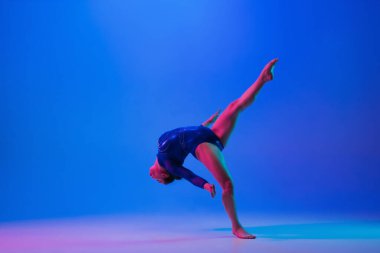 Genç esnek kız mavi stüdyo arka planında izole edilmiş. Genç bayan model sanatsal jimnastik yapıyor. Esneklik ve denge egzersizleri.