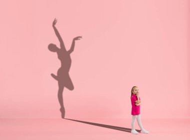 Çocukluk ve büyük ve ünlü bir gelecek hayal etmek. Kızlı kavramsal imaj ve mercan pembe arka planda formda kadın balerin gölgesi.