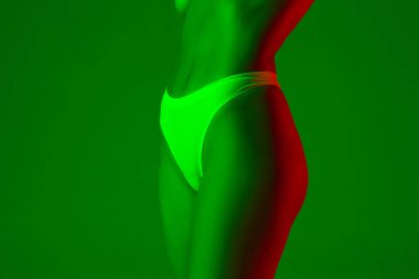 Neon ışıkta yeşil arka planda güzel bir kadın göbeği. Güzellik, kozmetik, spa, epilasyon, diyet ve tedavi, fitness konsepti.