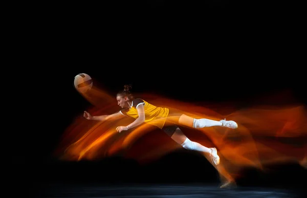 Jeune joueuse de volley isolée sur fond de studio noir. Femme dans l'entraînement d'équipement de sport et la pratique avec l'ombre du feu derrière elle — Photo