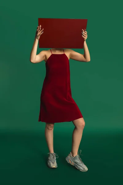 Female model in red outfit on green background with mirror. Style and beauty concept. Close up.