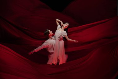 Genç ve zarif bale dansçıları klasik hareketlerde kırmızı bez üzerinde dalgalanan arka planda. Sanat, hareket, eylem, esneklik, ilham kavramı.