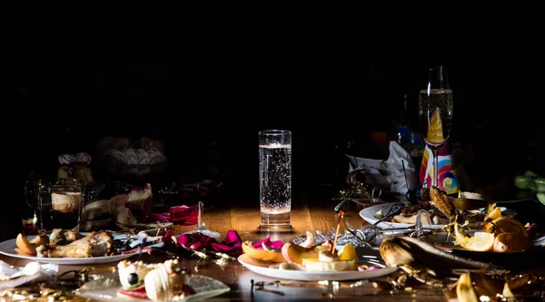 Early morning after the party. Glass of pure, cold water on the table with confetti and serpentine, leftovers, flower petals