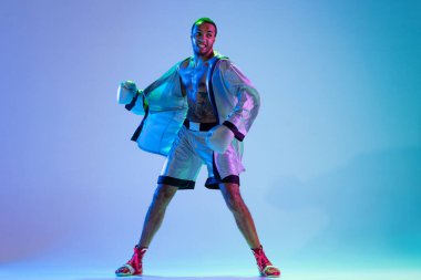 Beyaz kıyafetli, havalı bir adam volta atıyor. Neon ışıklı arka planda değişkenlik gösteriyor.